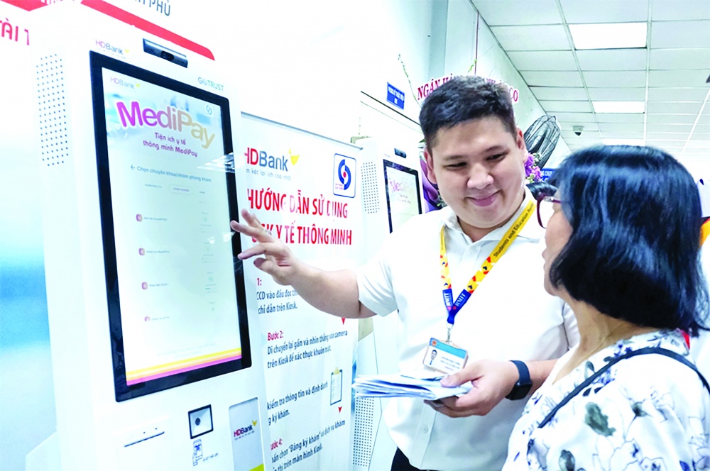 Người dân được nhân viên ở một cơ sở y tế hướng dẫn đăng ký khám chữa bệnh trên Kiosk y tế điện tử 